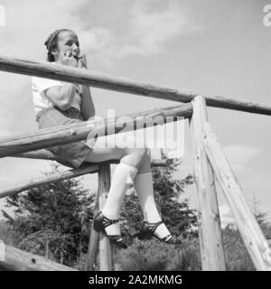 Eine Frau sitzt in einem Zaun und spielt Mundharmonika, Deutschland 1930er Jahre. Eine junge Frau sitzt auf einem Zaun und spielen eine Mundharmonika, Deutschland 1930. Stockfoto