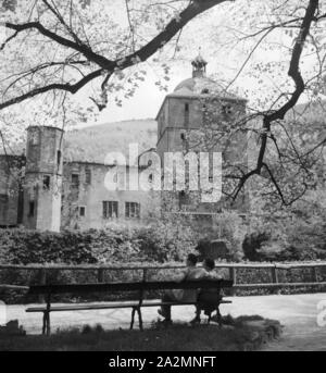 Ein Paar sitzt auf einer Bank vor dem Schloss in Heidelberg, Deutschland 1930er Jahre. Ein paar sitzen auf einer Bank am Heidelberger Schloss, Deutschland 1930. Stockfoto