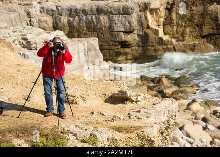 Ein Fotograf an einem windigen Tag fotografieren mit einem Stativ auf den Klippen von Portland Bill, Isle of Portland England UK GB Stockfoto