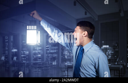 Schreien Geschäftsmann Holding leuchtende Laterne auf Hintergrund office Interieur. Seitenansicht der emotionalen Mann in Hemd und Krawatte auf der Suche nach Etwas in dunklen Stockfoto