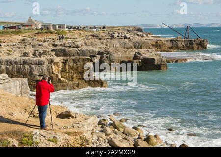 Ein Fotograf an einem windigen Tag fotografieren mit einem Stativ auf den Klippen von Portland Bill, Isle of Portland England UK GB Stockfoto