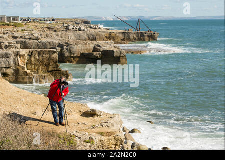 Ein Fotograf an einem windigen Tag fotografieren mit einem Stativ auf den Klippen von Portland Bill, Isle of Portland England UK GB Stockfoto