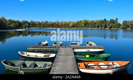 Herbst Landschaft. Ein See, ein Boot Brücke und einige Boote mit gelben und grünen Bäumen im Hintergrund. 68782 Bruehl, Baden-Württemberg, Deutschland. Stockfoto