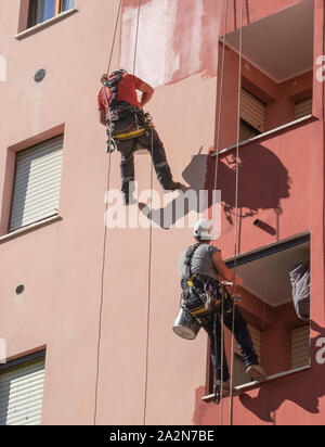 Bauarbeiter senken sich auf die Fassade eines Gebäudes mit Seilen für Wartung Stockfoto