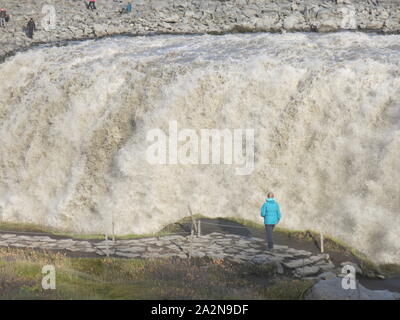 Ein einsamer Tourist auf den Stein weg ist durch die Skala und das Volumen des Wassers an Dettifoss, Islands größten Wasserfall in den Schatten gestellt. Stockfoto