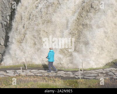 Ein einsamer Tourist auf den Stein weg ist durch die Skala und das Volumen des Wassers an Dettifoss, Islands größten Wasserfall in den Schatten gestellt. Stockfoto