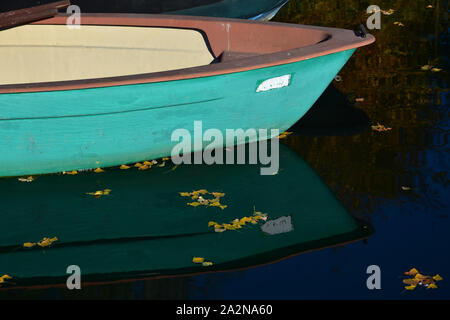 Der vordere Teil des grünen Boot im See, im Wasser widerspiegelt. Einige gelbe Blätter sind auf der Wasseroberfläche. Stockfoto