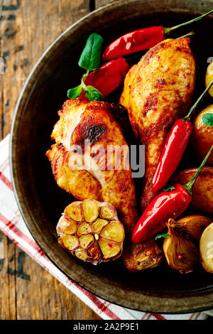 Würzige Hähnchenkeulen mit gebackenen Kartoffeln, Knoblauch, Chili, Paprika und frischen Kräutern. Hausgemachte Speisen. Stockfoto