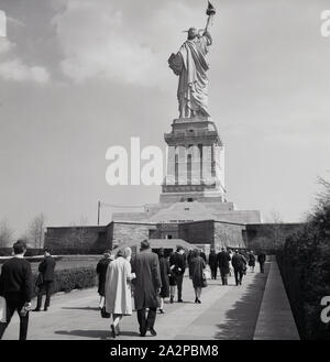 Die 1960er Jahre sind historisch. Besucher, die einen Weg zur Freiheitsstatue, einer kolossalen neoklassizistischen Skulptur auf Liberty Island im New York Harbour in New York City, USA, Unternehmen. Die Kupferstatue war ein Geschenk des französischen Volkes. Die Metallkonstruktion wurde von dem französischen Bildhauer Frédéric Auguste Bartholdi entworfen und von Gustave Eiffel, er, dem berühmten Pariser Turm, erbaut. Stockfoto