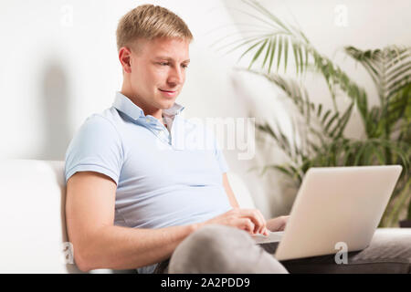 Freundliche junge Mann am Laptop zu Hause arbeiten. Stockfoto