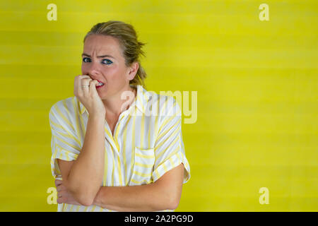 Frau, die an isolierten gelb Hintergrund gestresst und nervös mit den Händen in den Mund beißen Ihre Nägel. Angst problem - Bild Stockfoto