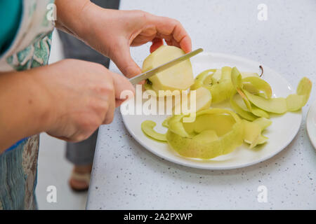Direkt oberhalb der Schoß der Frau Peeling ein Apple. Die Frau klopft oben auf dem Apple. Weibliche Hände Peeling Haut aus der Green Apple mit einem Schälbohrer Stockfoto