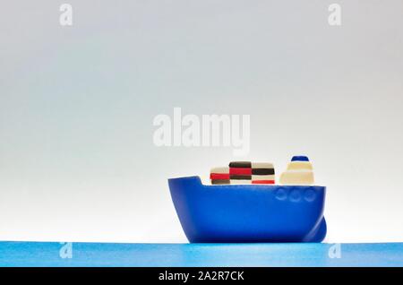 Toy Blue Schiff bunten Containern segeln über den Horizont mit einem einfachen Hintergrund und Platz für Text. Stockfoto