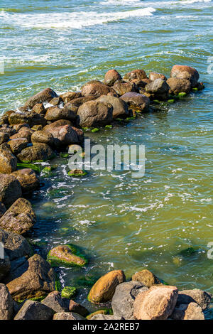 Nahaufnahme eines Wellenbrechers aus riesigen Felsbrocken, Ostsee, in Palanga, Litauen, Europa. Grüne Ostsee Wasser bricht den Stein groyne. Stockfoto