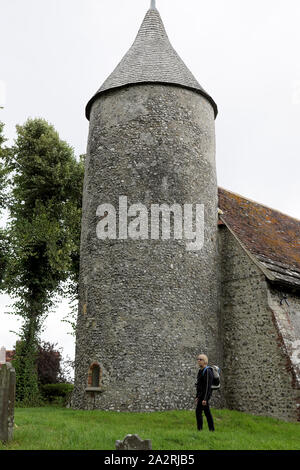 Eine Frau Wanderer mit Rucksack steht neben der Kirche St. Peter, runden Turm in der Southease Dorf East Sussex, England UK KATHY DEWITT Stockfoto