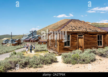 Menschen entdecken Bodie State Historic Park mit dem Standard konsolidierte Mining Company Stamp Mill im Hintergrund und ein altes Holzhaus neben der Stockfoto