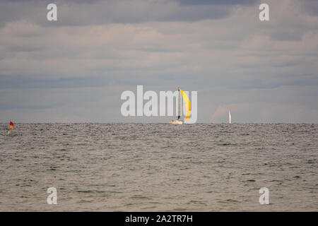 Weit auf das Meer schwebt ein Segelboot mit einer leuchtend gelben Segeln und der Himmel ist voller Wolken Stockfoto