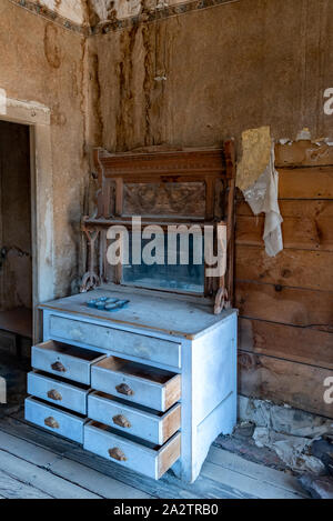 Leere verlassene Kommode mit Spiegel in Tom Miller Haus in Bodie State Historic Park. Reste von Tapeten schälen und hängen Rom die Wand. Stockfoto