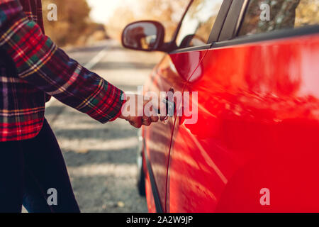 Öffnen der Kabinentür. Frau öffnet rotes Auto mit Schlüssel auf Herbst Straße Stockfoto