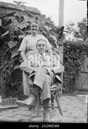 Glas Negativ - Paar in Garten, circa 1920s - 1930s, Schwarz und Weiß 1/6 Platte Glas negative von ein Paar in einem Garten oder Innenhof. Der Mann sitzt im Schneidersitz auf einem Stuhl und die Frau hinter ihm steht. Sammlung von Produkten, Werbematerialien, Fotos und Arbeitsleben Artefakte, wenn die Melbourne Produktionsanlage am Standort Coburg geschlossen Stockfoto