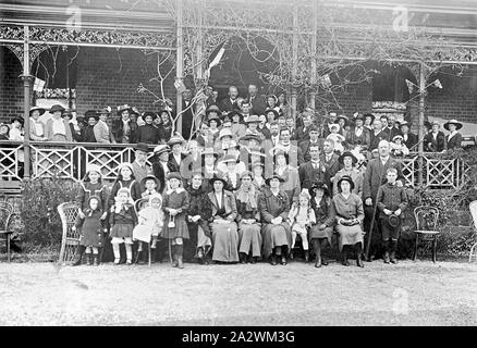 Negative - große Gruppe auf der Veranda & Vor Elaine Coursing Club, Elaine, Victoria, ca. 1925, eine große Gruppe von Menschen, die auf der Veranda und vor der Elaine Coursing Club Gebäude. Die Veranda ist mit schmiedeeisernen Spitze, und es ist eine Pflanze, um dieser wachsenden. Das Haus ist aus Ziegelsteinen gemauert, und zwei großen Fenstern kann auf beiden Seiten des großen Tür gesehen werden. Viele der Leute, die tragen Hüte, die Frauen tragen Kleider und die Männer tragen Anzüge und Krawatten. Es gibt mehrere Stockfoto