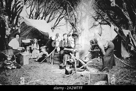 Negative - Gippsland, Victoria, um 1910, ein Camp mit ein Mann, drei Frauen und vier Kinder. Eine Frau ist das Kochen am Lagerfeuer, während der Mann hält eine Schale zu ein Fass. Es gibt verschiedene Utensilien aus Ästen ausgesetzt. Es gibt ein paar Waffen lehnte sich gegen eines der Zelte Stockfoto