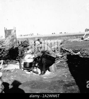 Negative - Red Cliffs, Victoria, 1922, Frau Martin Kochen im Freien auf einem Siedler blockieren. Eine Struktur, die auf der linken Seite erscheint eine Außentoilette. Stockfoto