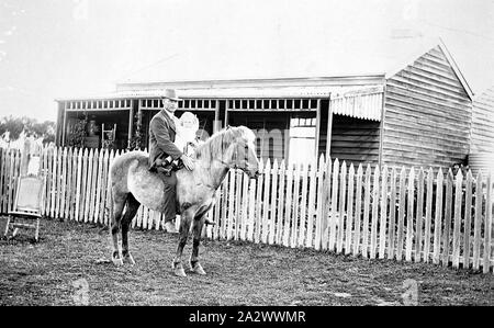 Negative - Maffra, Victoria, 1916, ein Mann auf dem Pferd. Er ist Reiten ohne Sattel und hält ein kleines Kind vor ihm. Es ist ein Holzhaus hinter Ihnen Stockfoto