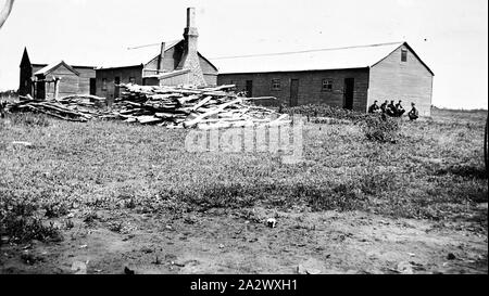 Negative - balranald District, New South Wales, etwa 1925, die Scheren auf 'Paika' Bahnhof werfen. Es ist ein Stack von Brennholz im Vordergrund und eine Gruppe von Männern sitzt auf der rechten Seite Stockfoto