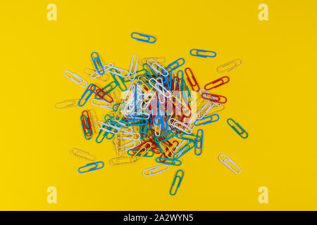 Ein Haufen von farbigen Büroklammern auf eine gelbe Fläche verstreut Stockfoto