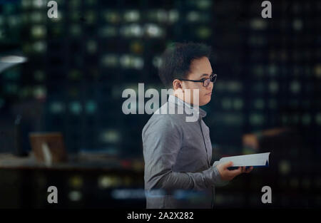 Junger Mann mit langen Ärmeln und Brillen vorübergehend an etwas anderes abgelenkt und Gedanken über etwas, während ein Buch zu lesen. Stockfoto