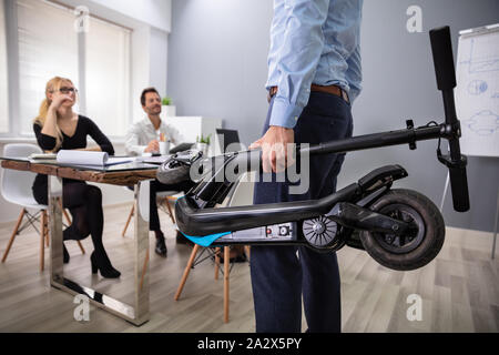 Unternehmer, die gefaltet Elektroroller Vor seinen Kollegen im Büro Stockfoto