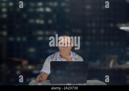 Ernsthafte Kerl. Und denken sehr konzentrieren. Mann im Büro vor seinem Laptop in der Nachtschicht arbeiten. Ein Büro Job eine Nacht. Stockfoto