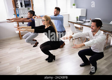 Lächelnd multi-ethnische junge Geschäftsleute tun, Sit-ups zusammen am Arbeitsplatz Stockfoto