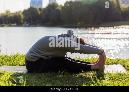 Man Yoga Asanas im City Park inspiriert. Fitness im Freien und Life Balance Konzept. Stockfoto