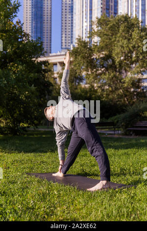 Man Yoga Asanas im City Park inspiriert. Fitness im Freien und Life Balance Konzept. Stretching. Dreieck Pose oder Trikonasana Stockfoto