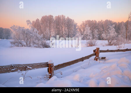 Sibirische ländlichen Winterlandschaft. Dawn in die Landschaft. Holzbalken Zaun auf Vorder- und Bäume mit Raureif auf Hintergrund Stockfoto