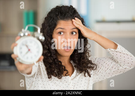 Junge Frau suchen terrified Holding einen Wecker Stockfoto