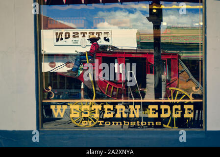 Die westliche Flanke von Tombstone Modellbahn shop, hat eine Reflexion in der Storefront Fenster eines roten Postkutsche durch in Tombstone, AZ, USA fahren Stockfoto