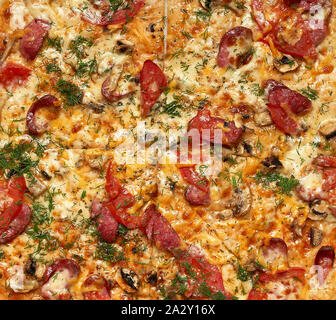 Gebackene Pizza mit geräuchertem Würstchen, Pilze, Tomaten, Käse und Dill, geschnitten Essen, Vollbild, Nahaufnahme Stockfoto