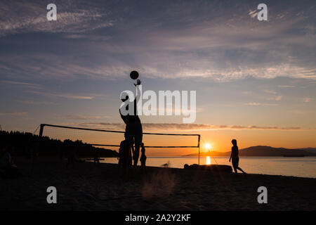 Eine Gruppe junger Leute, die Beachvolleyball spielten, spielten gegen den Sonnenuntergang am Kits Beach in Vancouver, BC. Stockfoto