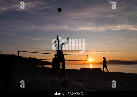Eine Gruppe junger Leute, die Beachvolleyball spielten, spielten gegen den Sonnenuntergang am Kits Beach in Vancouver, BC. Stockfoto