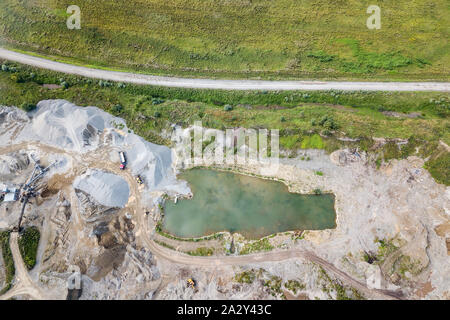 Luftaufnahme von einer kleinen Pflanze zur Produktion und Reinigung Schutt und Zement in der Nähe der Haufen von Baustoffen und Grube von Wasser, die Traktoren und Stockfoto
