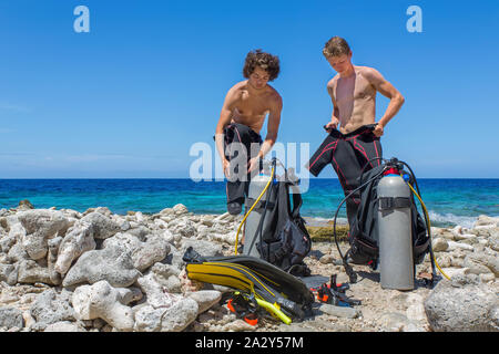 Zwei niederländische Taucher ändern Kleidung am Strand auf Bonaire mit blauen Meer Stockfoto