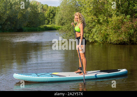Ständigen jungen kaukasischen Frau Plattenelektroden mit SUP auf dem Wasser des Flusses Stockfoto