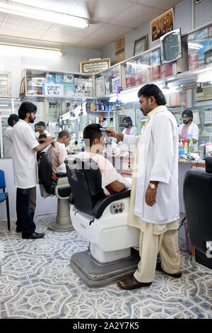 Arabisch Mann mit Bart bedeckt mit weißen Cape sitzt in Friseure Stuhl, Schönheit liefert Hintergrund. Mann mit Bart client der Hipster barbershop Stockfoto