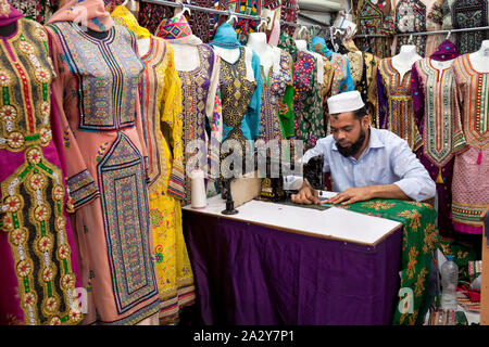 Ein Schneider in seinem Geschäft in Front an einer Nähmaschine mit bunten Kleider in Maskat, Oman, sitzen Stockfoto