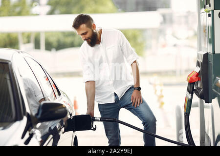 Mann, der an einer Tankstelle. Guy refuelong ein Auto. Mann in einem weißen Hemd. Stockfoto