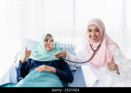 Eine junge Schöne muslimischen Arzt ist mit einem Stethoskop auf die Herzfrequenz des Patienten am Bett im Krankenhaus Untersuchungsraum zu hören. Stockfoto