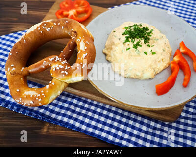 Traditionell bayerische Speisen Vorspeise mit Brezen und Käse Paste namens obazda auf Blau-weiß karierte Tischdecke und hölzerne Platte Stockfoto